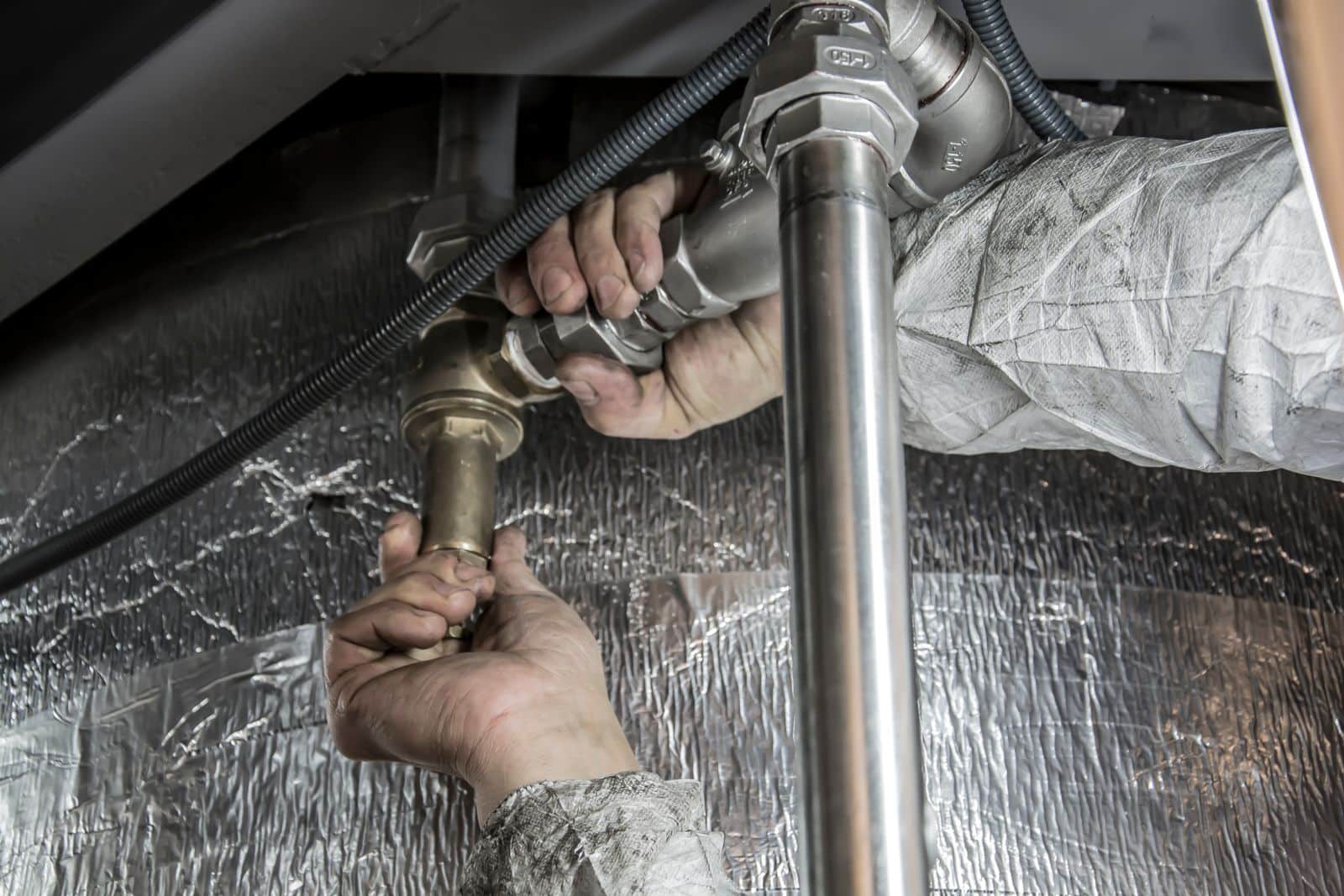 Handen van een loodgieter die metalen leidingen en koppelingen monteren